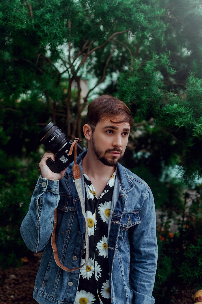 Crafting Captivating Headlines: Your awesome post title goes here A fashionable man in a floral shirt and denim jacket poses with a camera against a lush green backdrop.