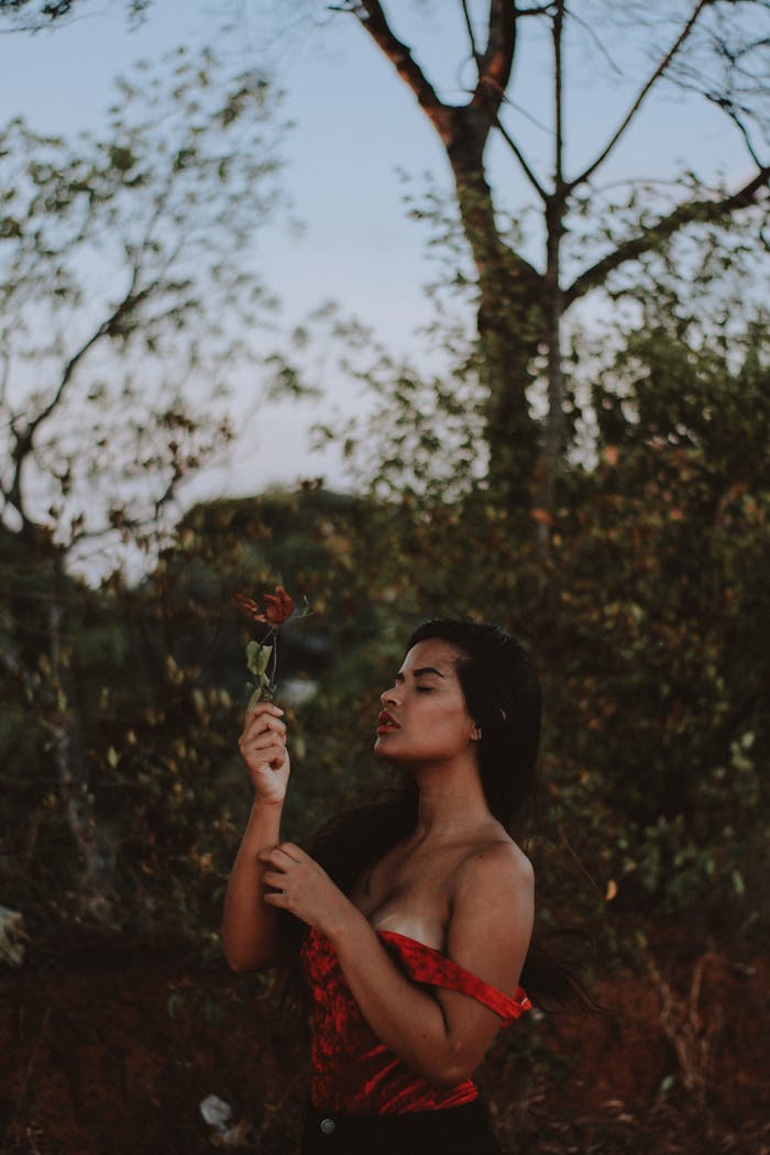 A woman in a red dress embraces nature in an outdoor portrait, capturing a serene moment in Brazil.